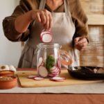 A woman preparing pickled radishes, showcasing ingredients in a rustic kitchen setting.