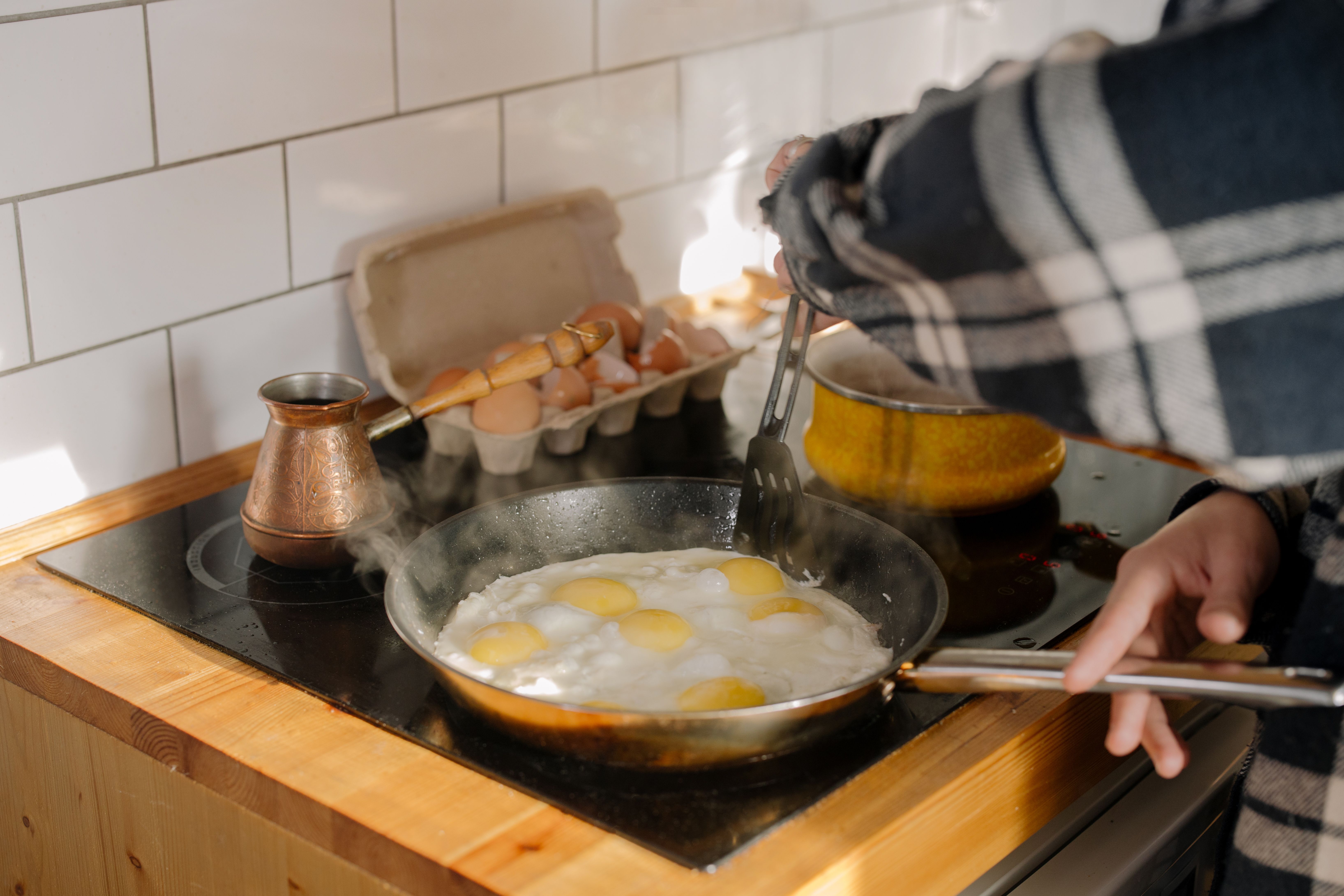 Close-up of cooking eggs on a stovetop with human hands in a kitchen setting.