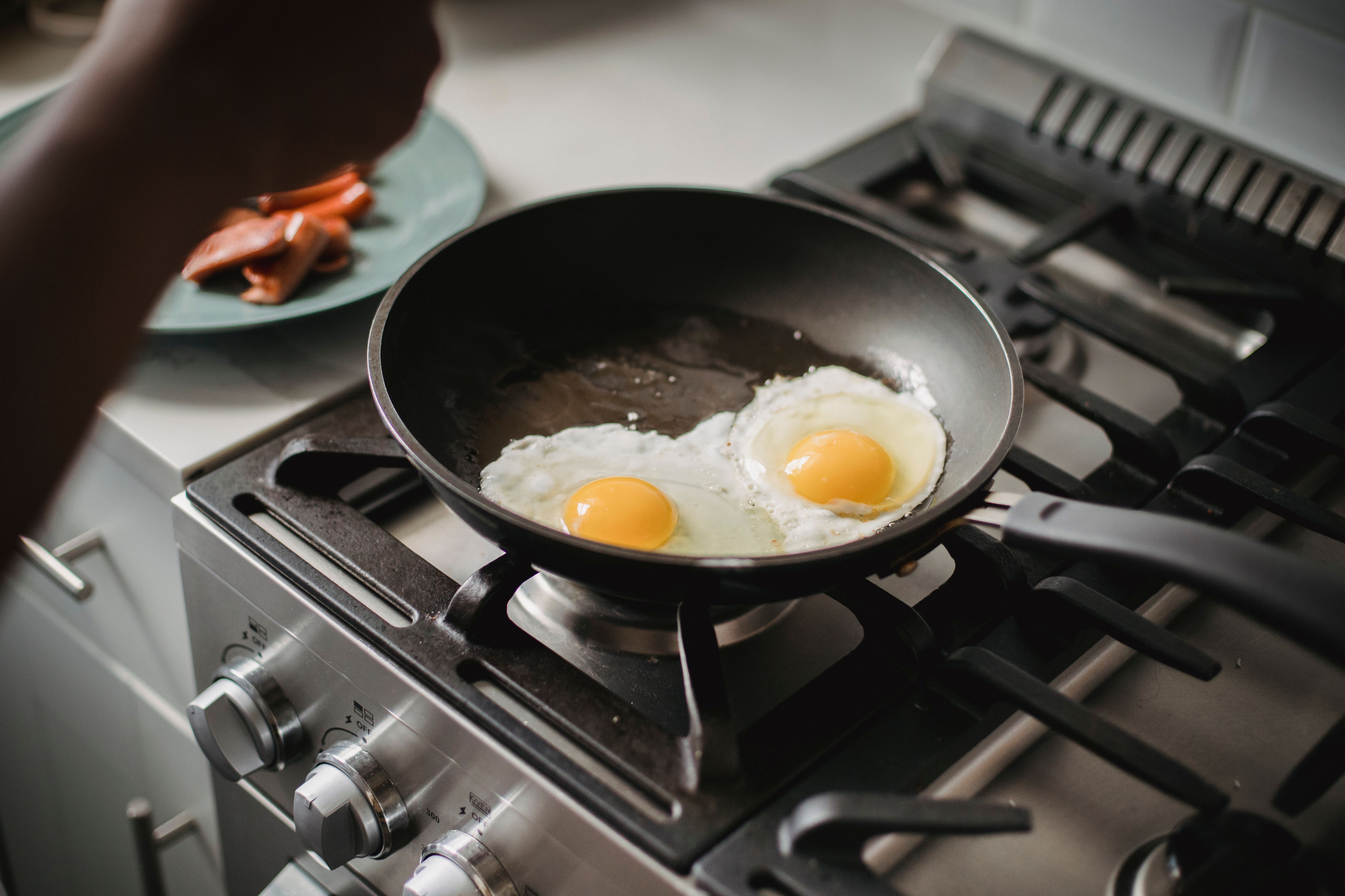 Close-up of two fried eggs cooking in a frying pan on a modern stovetop.